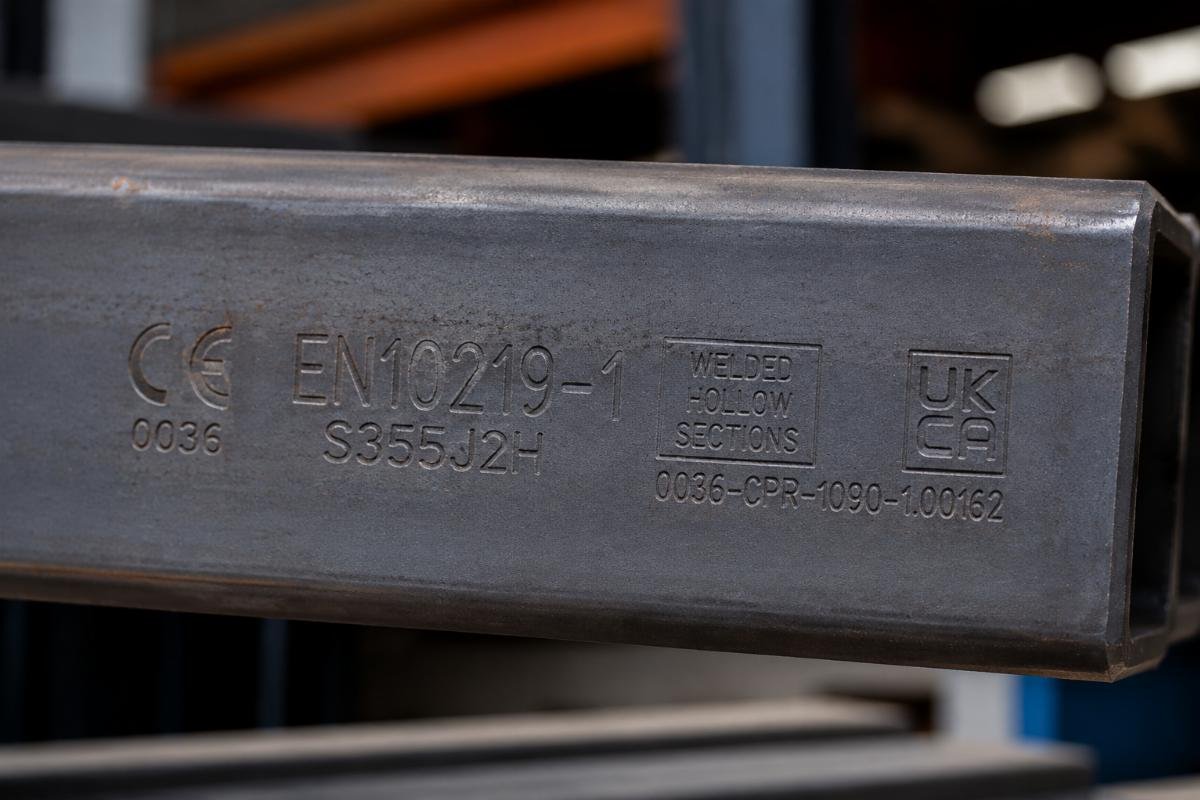 Close-up view of stamped identification on a steel beam showing EN10219 certification marks