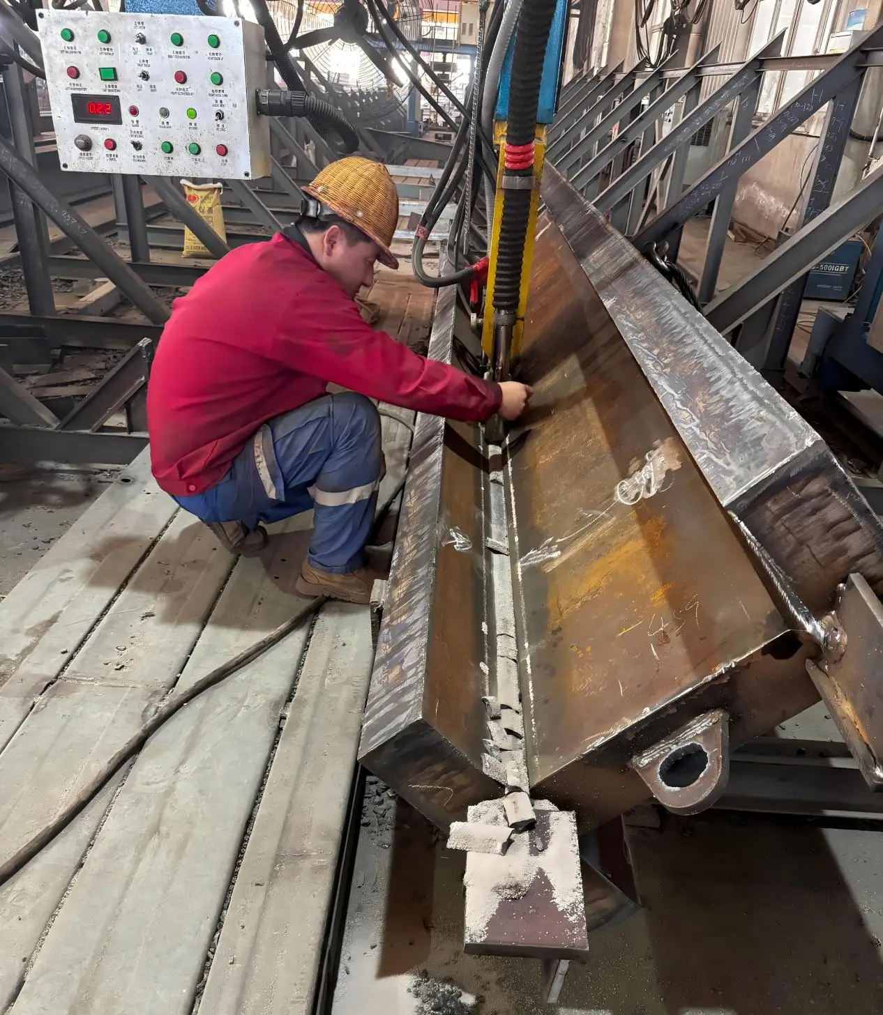 Welder performing submerged arc welding on heavy steel girder in fabrication workshop